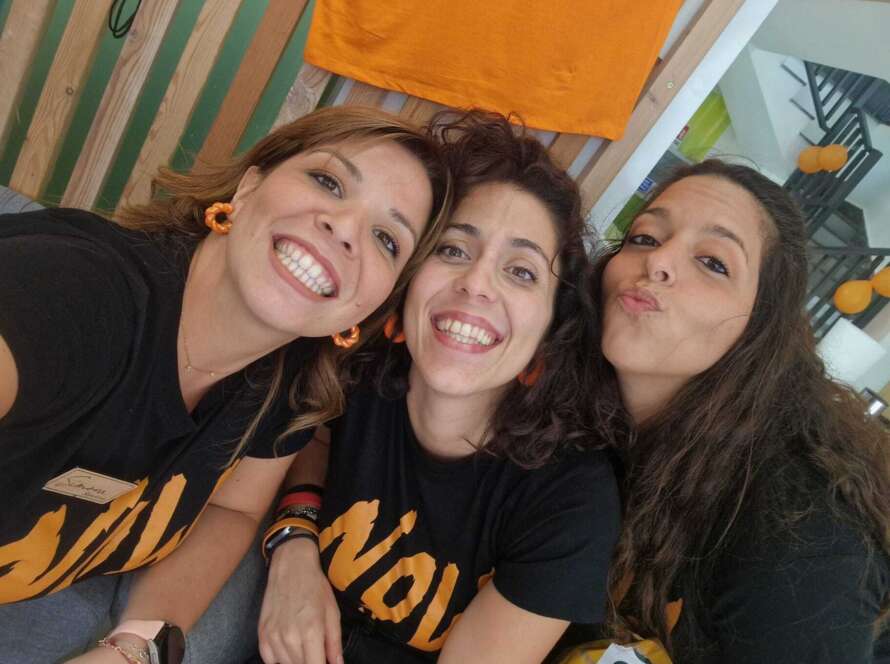 Tre donne in magliette arancioni e pantaloni neri sorridono.
