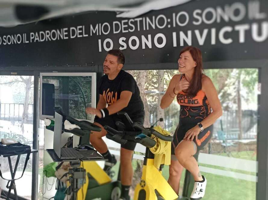 Due persone si allenano su biciclette in un'area all'aperto, con una tenda in vista.